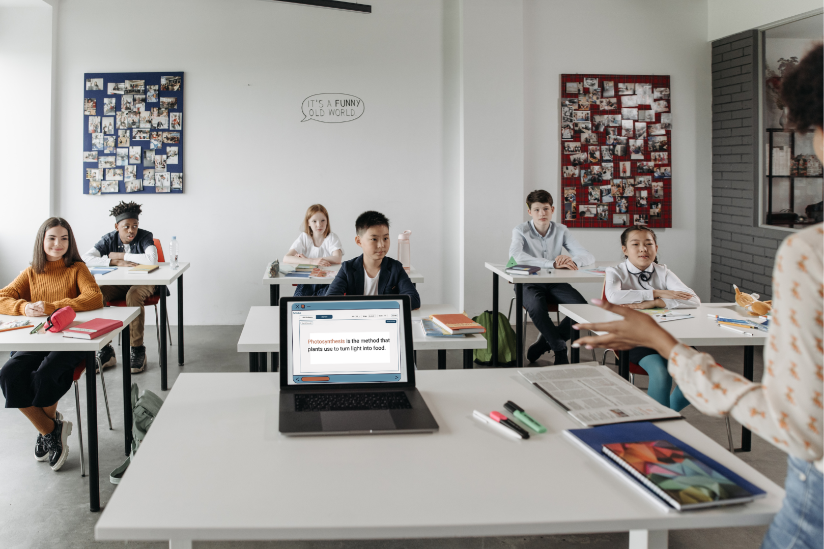 Teacher speaking in class while students read ReVerbal on a classroom laptop